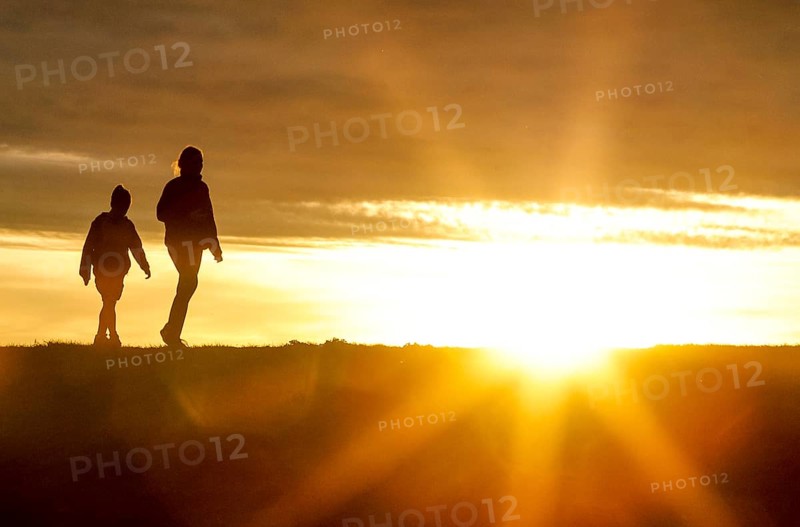 Woman and child walk across a dike on the island of Fehmarn at sunset, 13.10.2025, Fehmarn, Schleswig-Holstein, Germany