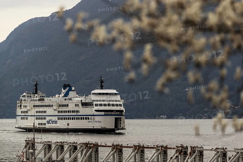 A large ferry on a calm body of water with mountains in the background under a cloudy sky in Horseshoe Bay, West Vancouver, British Columbia, Canada