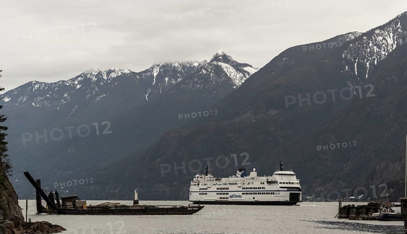 A ferry cruises through a scenic region with snowy mountains and cloudy skies in Horseshoe Bay, West Vancouver, British Columbia, Canada