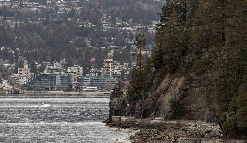 A rocky coastal path in Stanley Park with buildings and trees set against cloudy skies in Vancouver, British Columbia, Canada