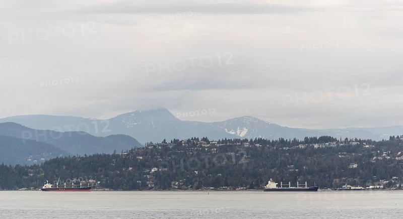 Distant view of ships passing by mountain-lined shores under cloudy skies in Vancouver, British Columbia, Canada