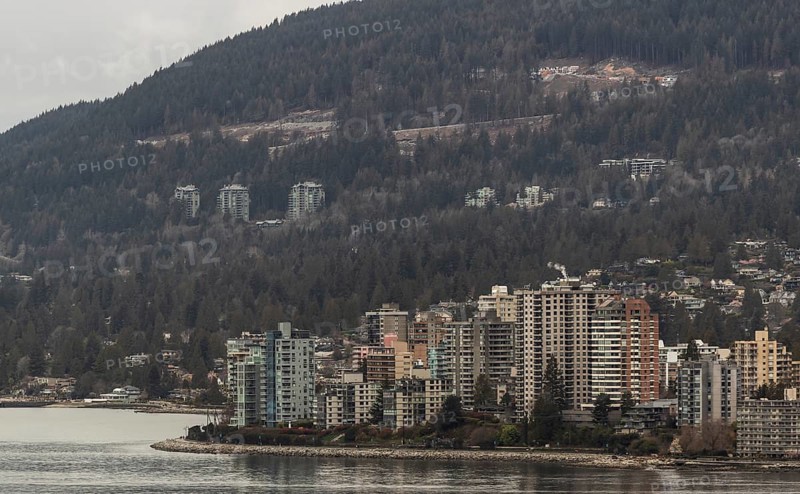 Urban high-rise buildings set against a backdrop of forest and mountains on an overcast day in Vancouver, British Columbia, Canada