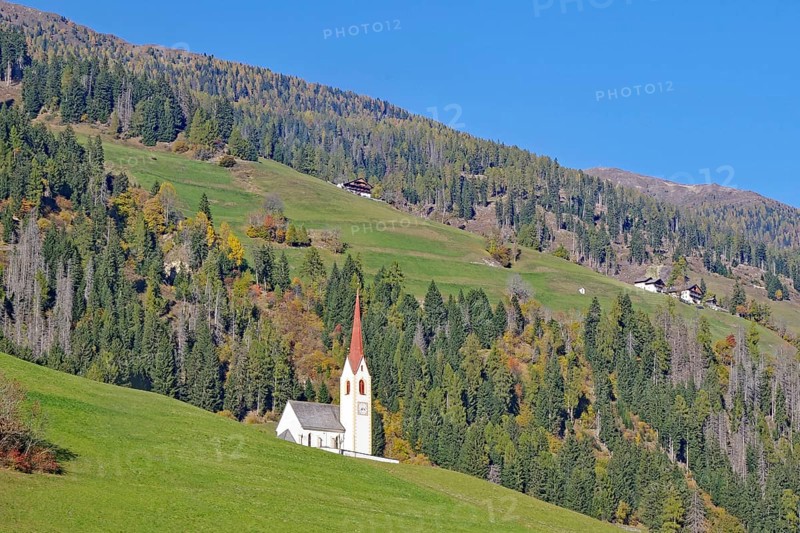 Lonely church with red tower on green alpine slope under bright blue sky, Dolomites, Drau cycle path, Tyrol, Italy