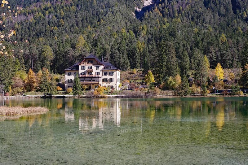 The villa is brilliantly reflected in a quiet alpine lake in front of dense forest and gentle slopes, Lake Toblach, Lake Dobbiaco, South Tyrol, Italy