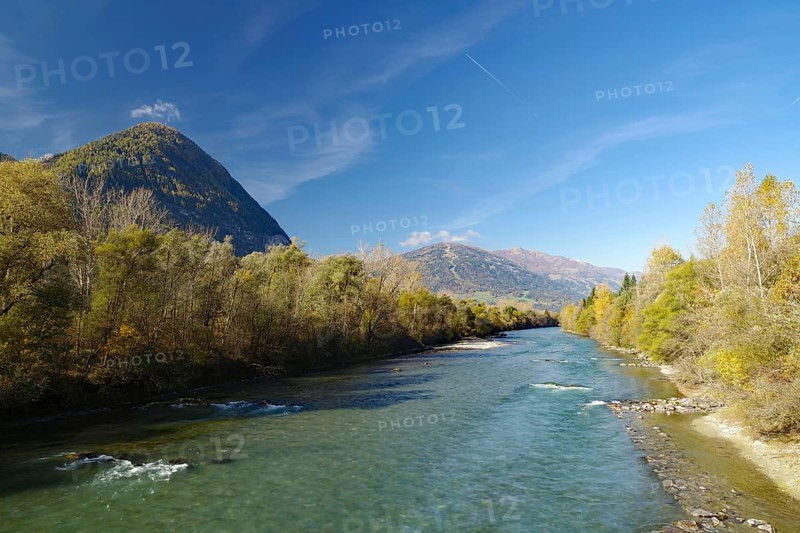 Wide river snakes through an autumnal valley, quiet sky with fine contrails, Lienz, Drau cycle path, Carinthia, Italy