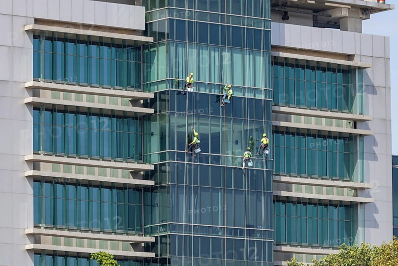 Window cleaners work as a team to clean the glass front of a hospital in downtown Bangkok, Thailand