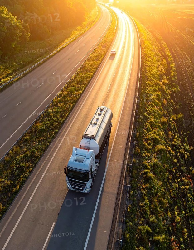 Petrol cargo truck lorry tanker driving on highway hauling oil products at sunrise, wide hilly landscape, AI generated