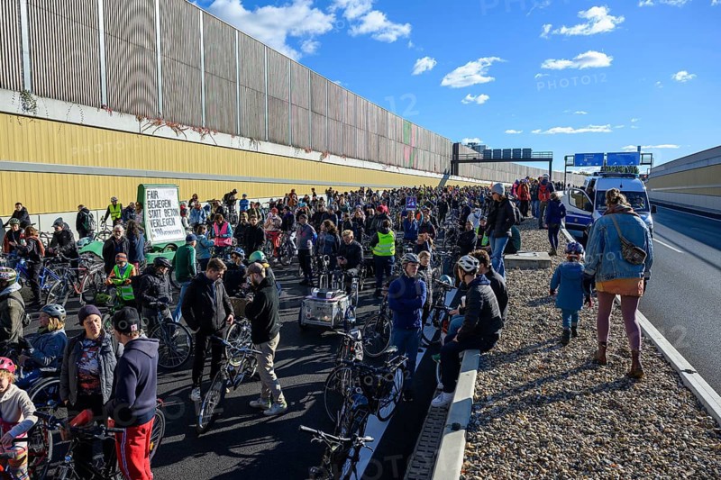 Cyclists at a demo on the 16th construction phase of the A100. Participants walk on the elevated central strip. Sign on a cargo bike: Move fairly instead of laying concrete. Berlin, 18.10.2025