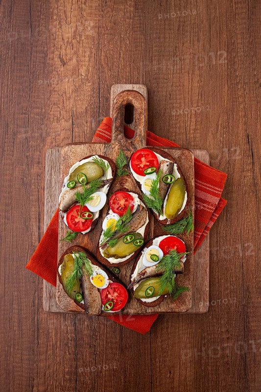 Sandwiches on rye bread with sprats, quail eggs, fresh tomatoes and pickled cucumber, on a wooden board, appetizer, breakfast