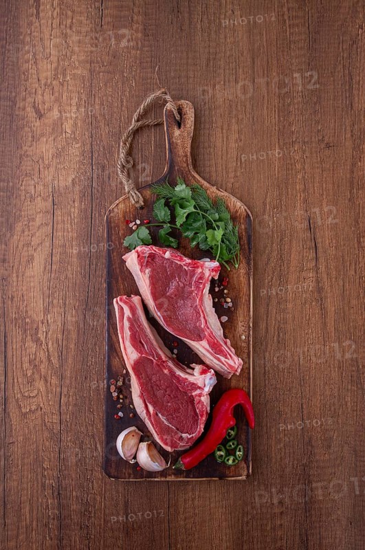 Freshly sliced lamb chops, with herbs and vegetables, on a wooden board, ready to cook, on a wooden table