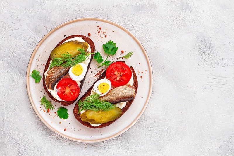 Sandwiches on rye bread, with sprats, quail eggs, fresh tomatoes and pickled cucumber, appetizer, breakfast, homemade