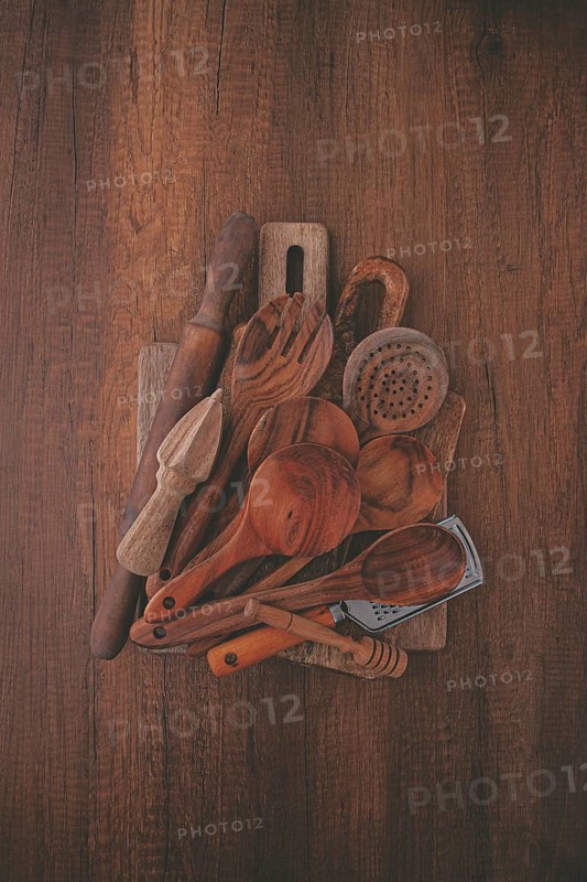A variety of wooden kitchen utensils are arranged on a dark brown wooden surface. Items include spoons, a spatula, and a rolling pin, showcasing their unique textures and shapes