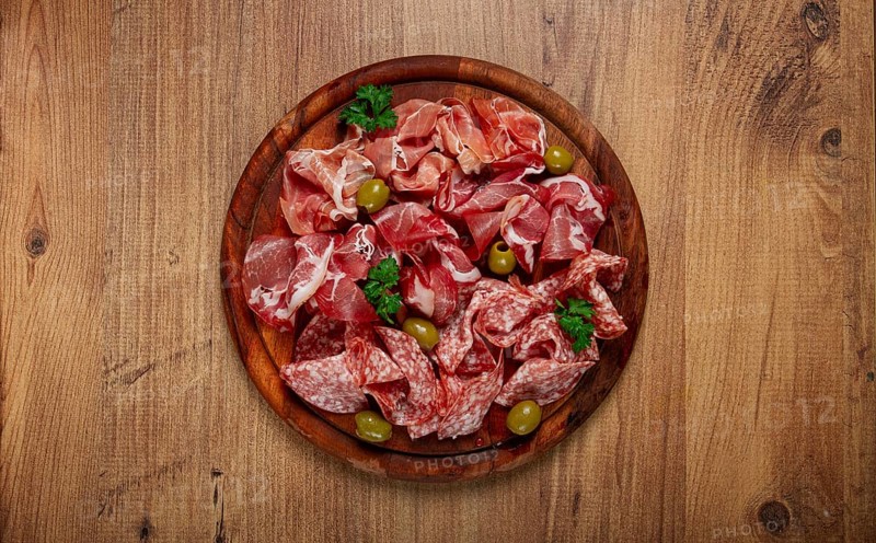 Assortment, sliced meat appetizer, prosciutto, salami and ham, with olives, on a wooden board, breakfast, top view, close-up, no people