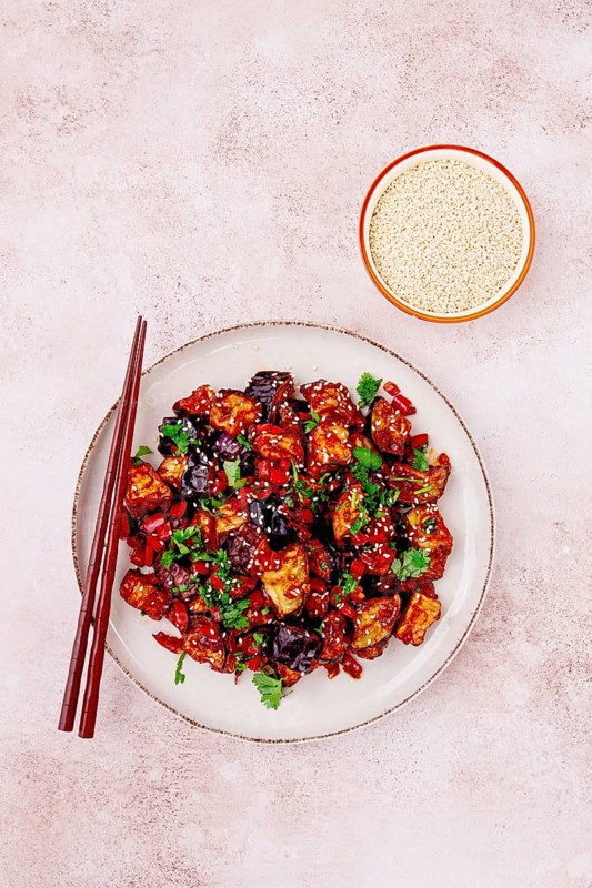 Fried eggplant, Chinese style, in sweet and sour sauce, with pepper and sesame seeds. on a white plate