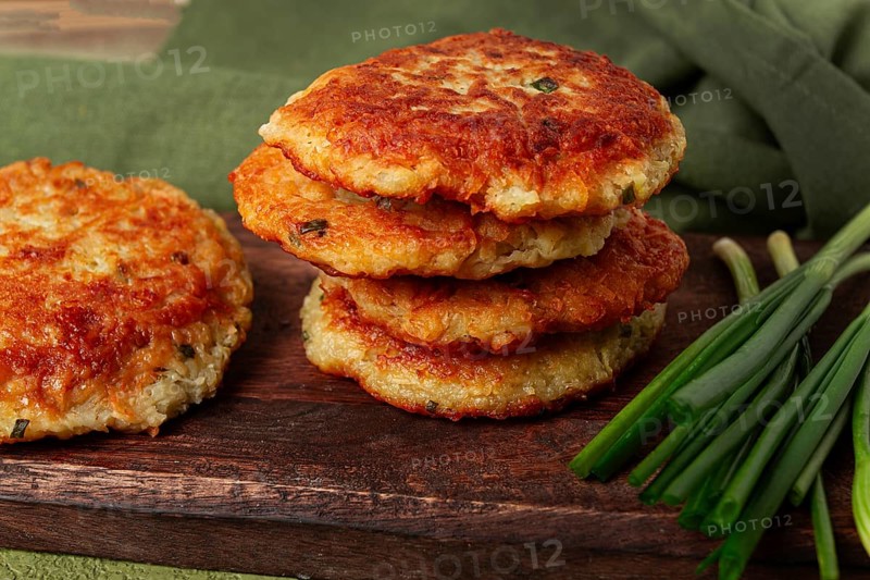 Crispy potato pancakes Latkes, stacked on a wooden board next to fresh green onions, natural light, homemade, no people
