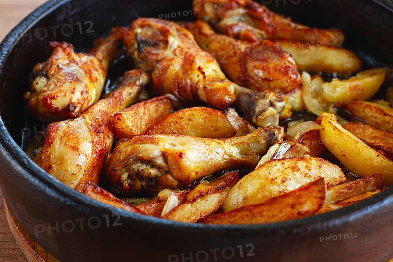 Fried chicken drumsticks with potato slices, in a clay pan, baked in the oven, with spices, homemade, no people