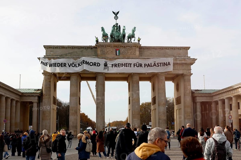 Several activists drop a banner with the inscription Never again genocide, freedom for Palestine and the Palestinian flag and set off pyrotechnics at the Brandenburg Gate, Berlin, 13.11.2025