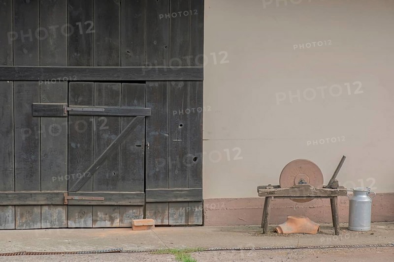 A whetstone and a bucket in front of an old rustic barn door, Hohwiller, Alsace, France