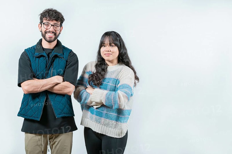 Smiling young couple with crossed arms looking at camera, isolated. Cheerful young multiethnic couple with arms crossed, isolated