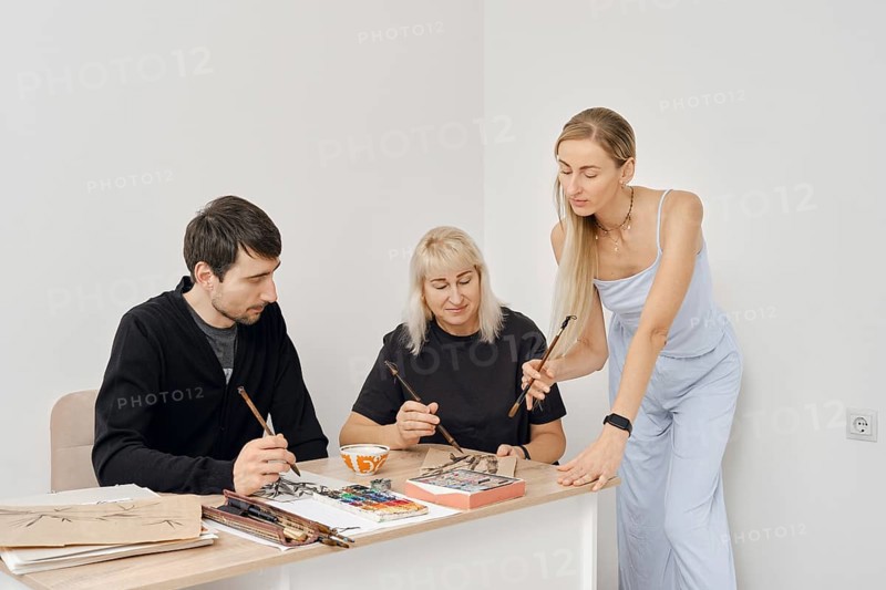 Three artists are engaged in a creative painting workshop. They share techniques and ideas while working on their projects at a bright, minimalist studio space during a sunny afternoon