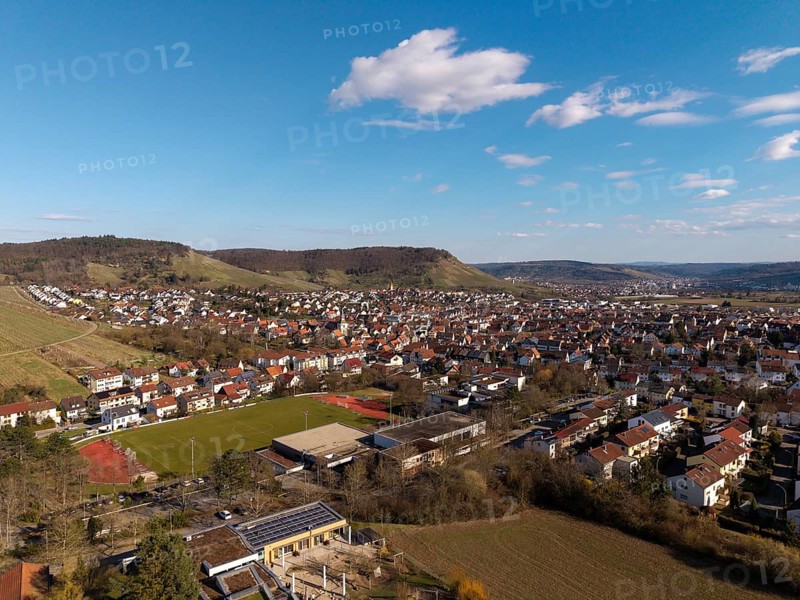 Large-scale city view with sports field in the foreground, surrounded by hills and blue skies, Korb im Remstal, Baden-Württemberg, Germany
