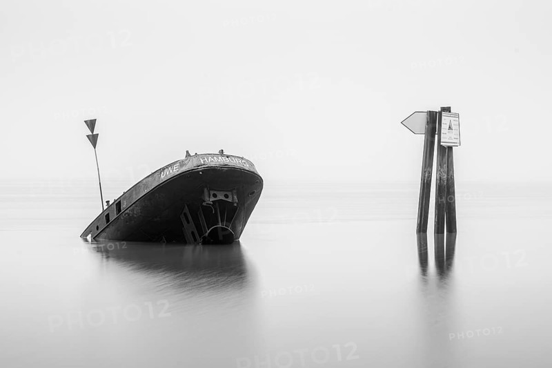 Long exposure of the partially sunken MS Uwe shipwreck in the Elbe on Falkensteiner Ufer in fog and calm water in black and white, Blankenese, Hamburg, Germany