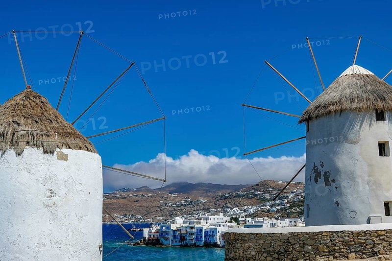 Mykonos, Cyclades, Greece - The six sixteenth-century windmills, lined up on a hill above Mykonos Town, Mykonos Chora, are the island's landmark. At the back, right by the sea, are the colorful houses of Little Venice. Mykonos is part of the Cyclades archipelago in the Aegean Sea