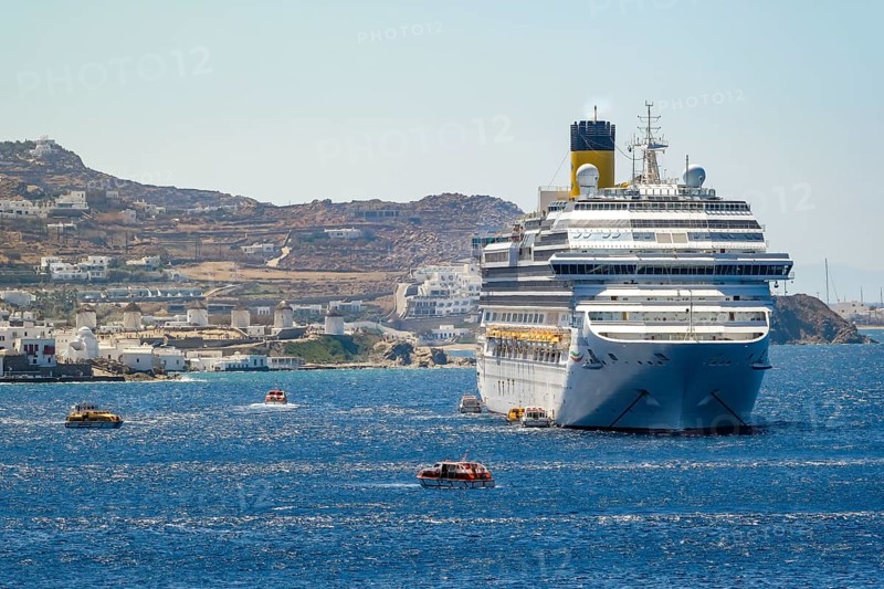 Mykonos, Cyclades, Greece - Cruise ship COSTA FORTUNA is located in the bay against the backdrop of the old town with the landmark of the six windmills, Mykonos Town. Cruise ships bring tourists to shore