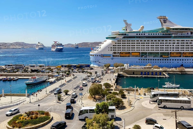 Mykonos, Cyclades, Greece - Mykonos New Port, cruise ship is moored on the quay in the new port in front of the skyline of Mykonos Town. At the back, there are more cruise ships in the bay off Mykonos City with a view of the old town with the windmills. Cruise ships bring tourists to the old town