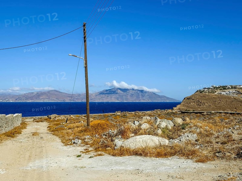 Mykonos, Cyclades, Greece - Barren landscape with street lamp on wooden pole, power pole, telephone pole. In the back is the island of Tinos