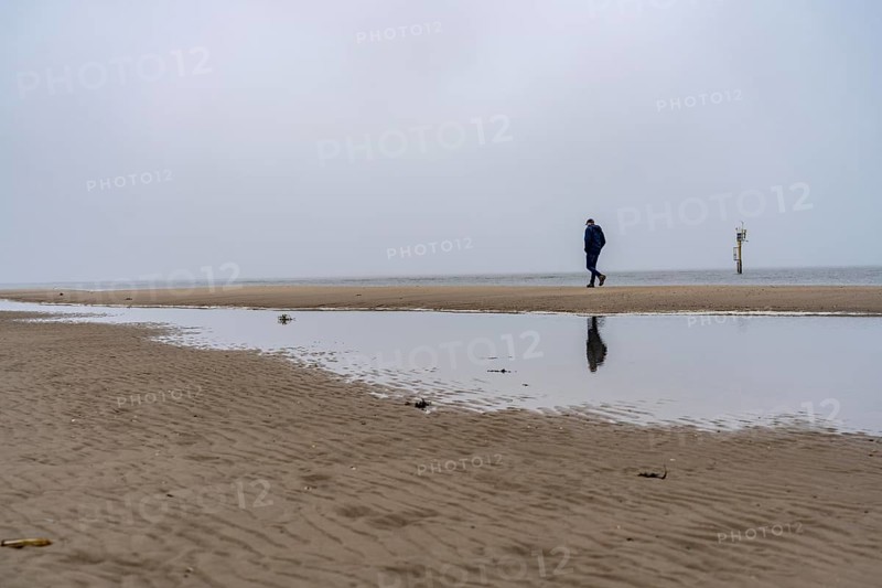 East beach of the East Frisian island of Spiekeroog, beach walk, man alone on the beach, at low tide, fog, calm of wind, tidal creek, Lower Saxony, Germany