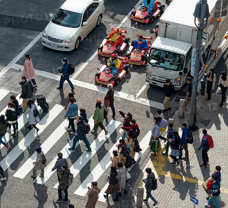 People cross zebra crossings, people in costumes ride small go-kart racing cars, Shibuya Crossing, Shibuya, Tokyo