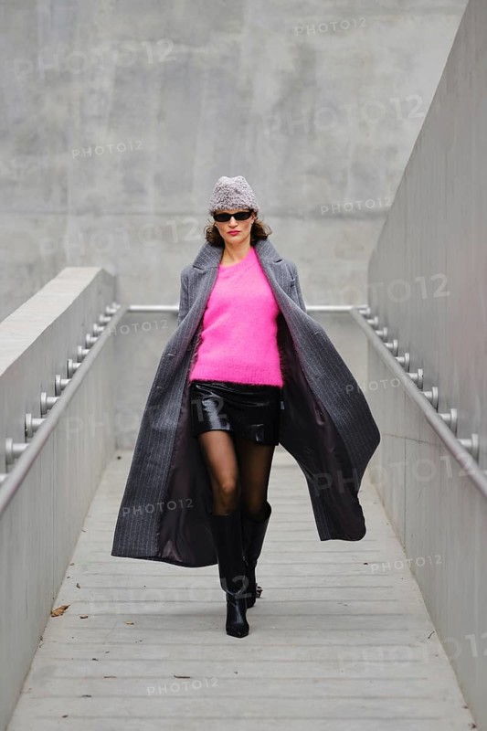 Model walks confidently in urban fashion featuring bright pink sweater and stylish coat