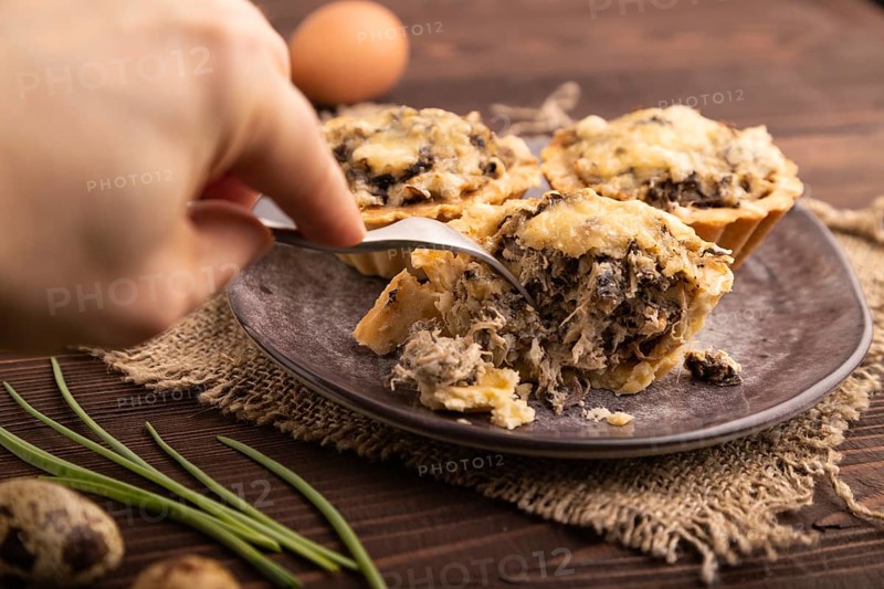 Tartlets with meat and cheese with hand on brown wooden background and linen textile. side view, close up, selective focus