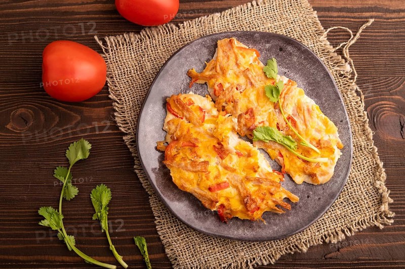 Baked chicken meat with cheese and tomatoes on brown wooden background and linen textile. top view, flat lay, copy space