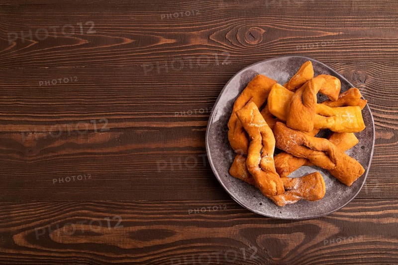 Crunchy biscuit Brushwood cookies sprinkled with powdered sugar on brown wooden background, top view, flat lay, copy space
