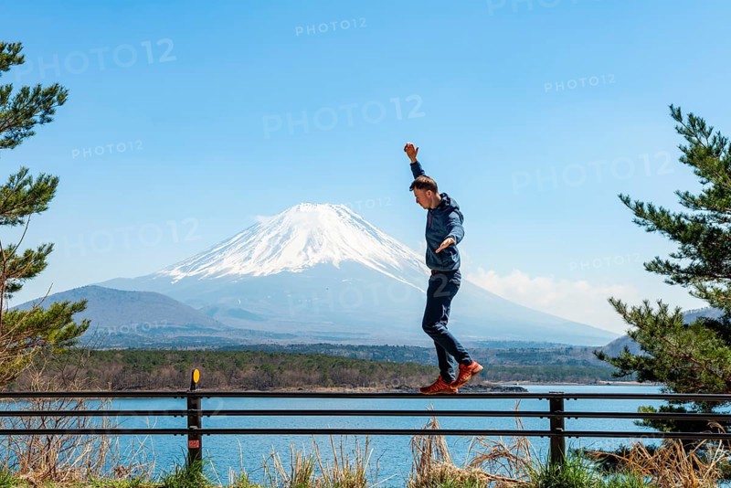 Young man balancing on railings next to a road, view across the lake to Mt Fuji volcano, Motosu Lake, Yamanashi Prefecture, Japan