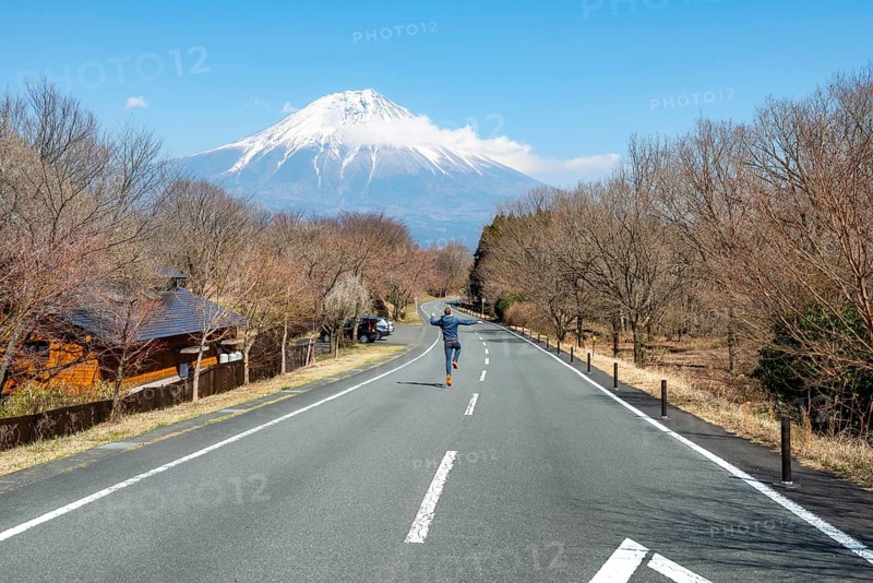 Young man jumping on road, road leading to Mount Fuji volcano, wanderlust, Yamanashi Prefecture, Japan