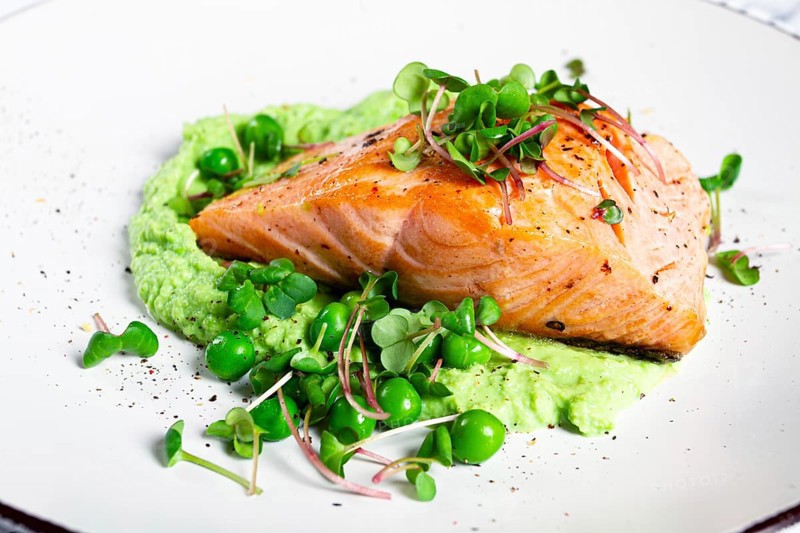 Delicious grilled salmon is placed elegantly on creamy green pea puree. Fresh microgreens and peas add a bright touch, creating an appetizing dish perfect for any meal