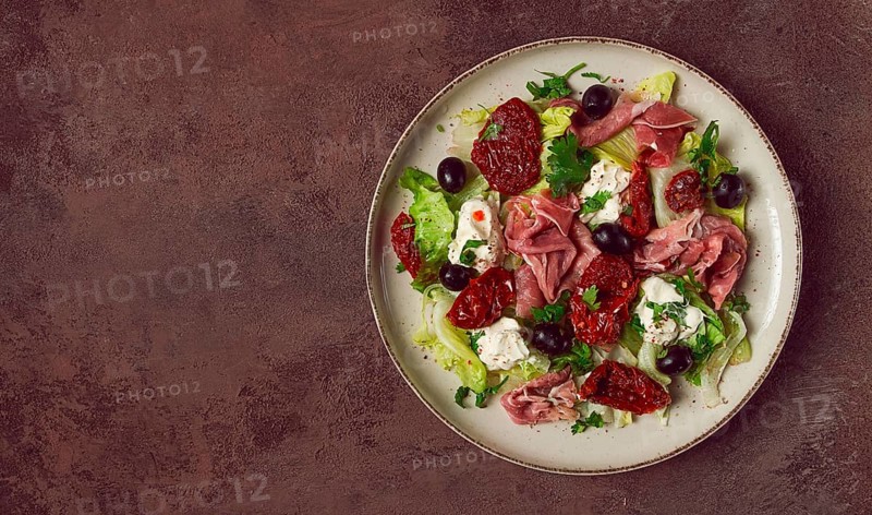 Salad with dried tomatoes, prosciutto, soft cheese, olives, homemade, top view