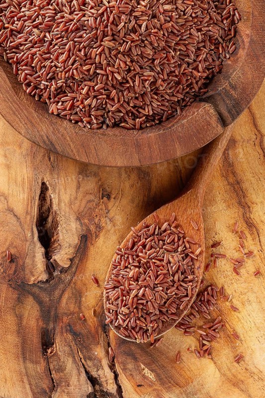 Natural, red rice, in a wooden bowl and spoon on a wooden surface in rustic style, top view