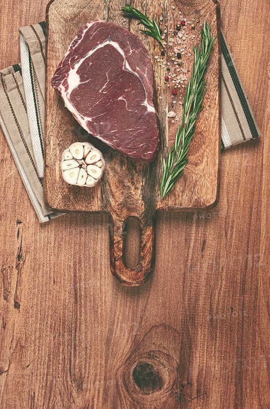 Raw steak, beef steak, rib eye steak, on a cutting board, freshly frozen, with spices and herbs, on the table, top view