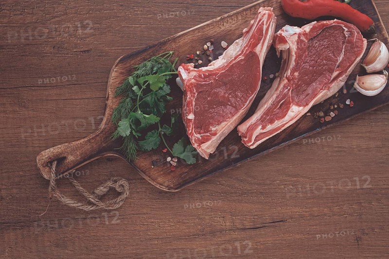 Freshly sliced lamb chops, with herbs and vegetables, on a wooden board, ready to cook, on a wooden table