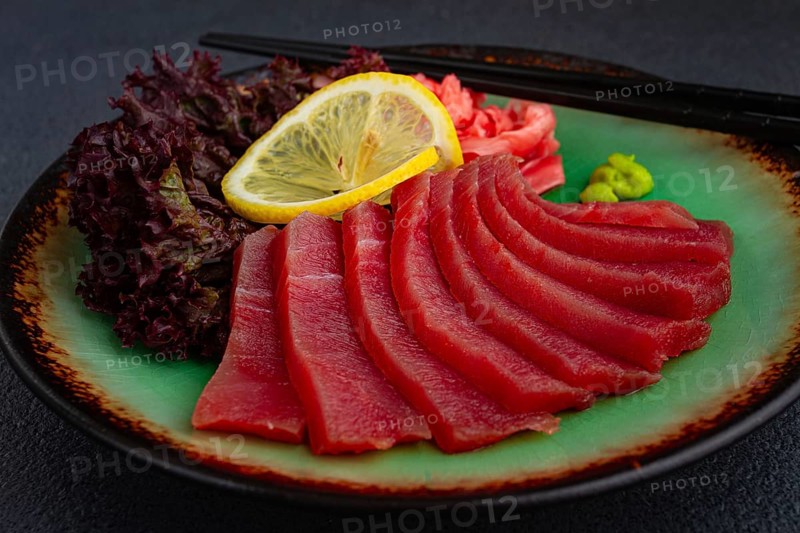 Fresh tuna sashimi served with lemon, wasabi, and pickled ginger on a dark background