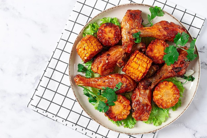 Fried chicken drumsticks, Mexican style, with corn, on a plate, close-up