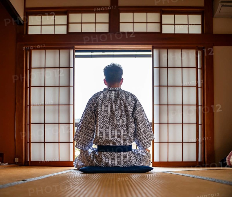 Young man wearing kimono sitting in traditional Japanese living room with tatami mats and shoji sliding doors, from behind, Yamanouchi, Nagano, Japan