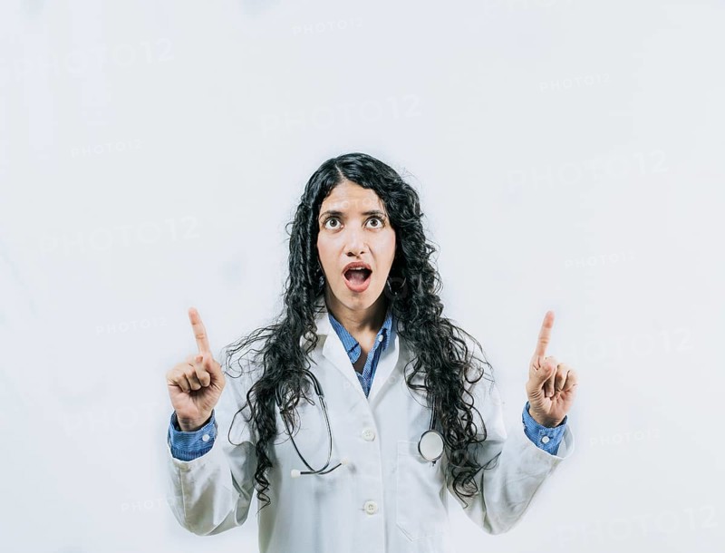 Young female doctor looking and pointing promotion up isolated. Surprised female doctor pointing up