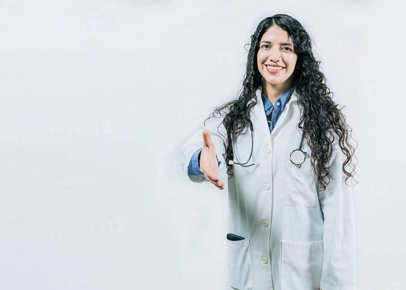 Smiling female doctor gesturing welcome, isolated. Latin female doctor shaking hands at the camera gesturing welcome
