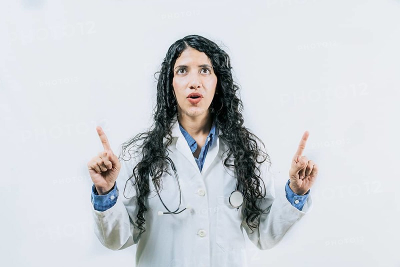 Surprised female doctor pointing up. Young female doctor looking and pointing promotion up isolated