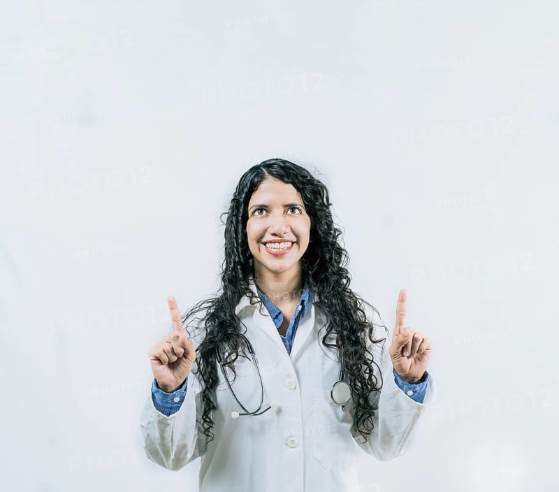 Cheerful female doctor pointing up isolated. Young female doctor looking and pointing at promotion up isolated